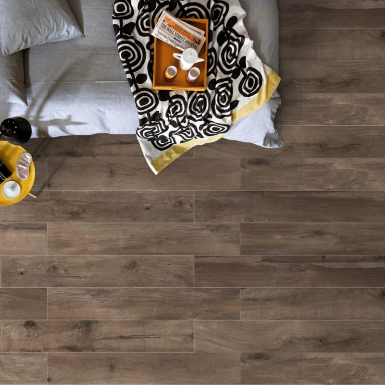 Overhead view of a Colville 8x48 Taupe wood-look porcelain floor beside a bed