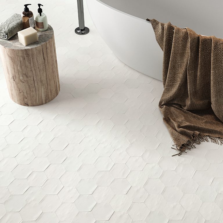 Switch 4x4-1/2 White hexagon tile floor beside a freestanding tub and wood stool