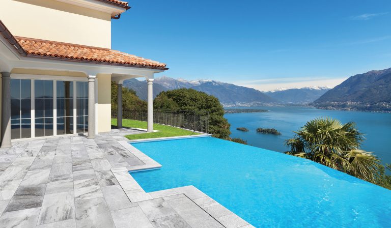 Infinity pool with a Niobe Gray fine-picked marble paver deck and modern edge coping overlooking a lake