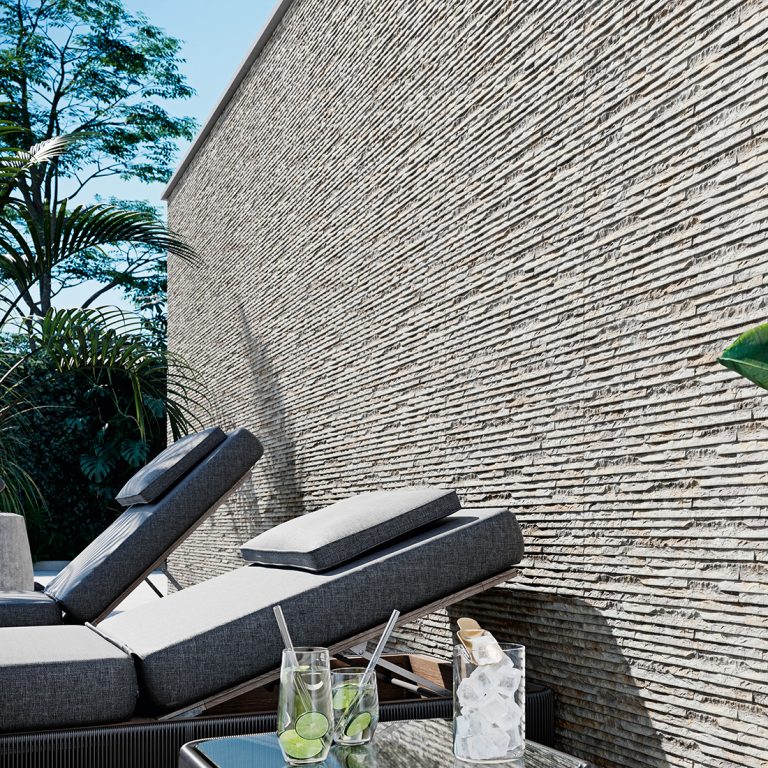Outdoor wall clad in Iguazu 8x25 Gray raked stone-look wall panels beside lounge chairs