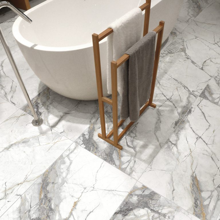 Bathroom floor in Invisible Gold 24x48 marble-look porcelain tile with a freestanding tub and towel rack