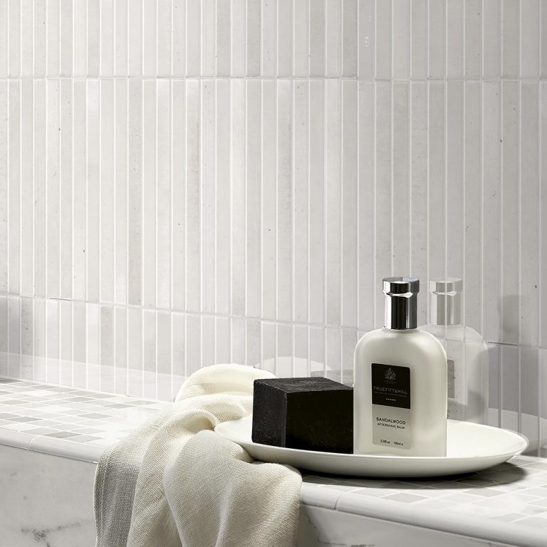 Bathroom wall in Posh Pitch 3D ivory glossy porcelain tile above a marble ledge with toiletries